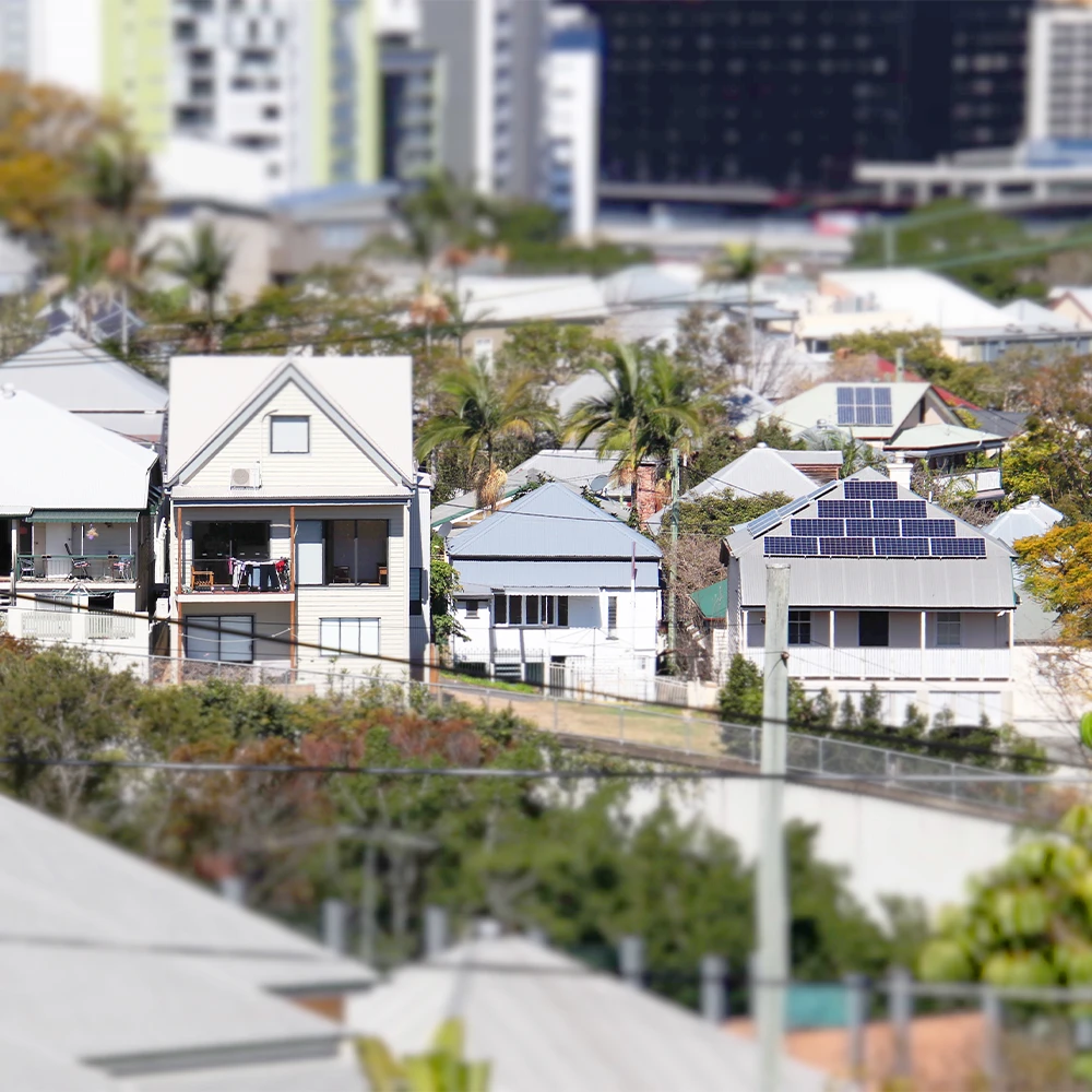 A view over rooftops and tree canopies to houses in an inner suburb of Brisbane, Australia. Some roofs have solar panels.